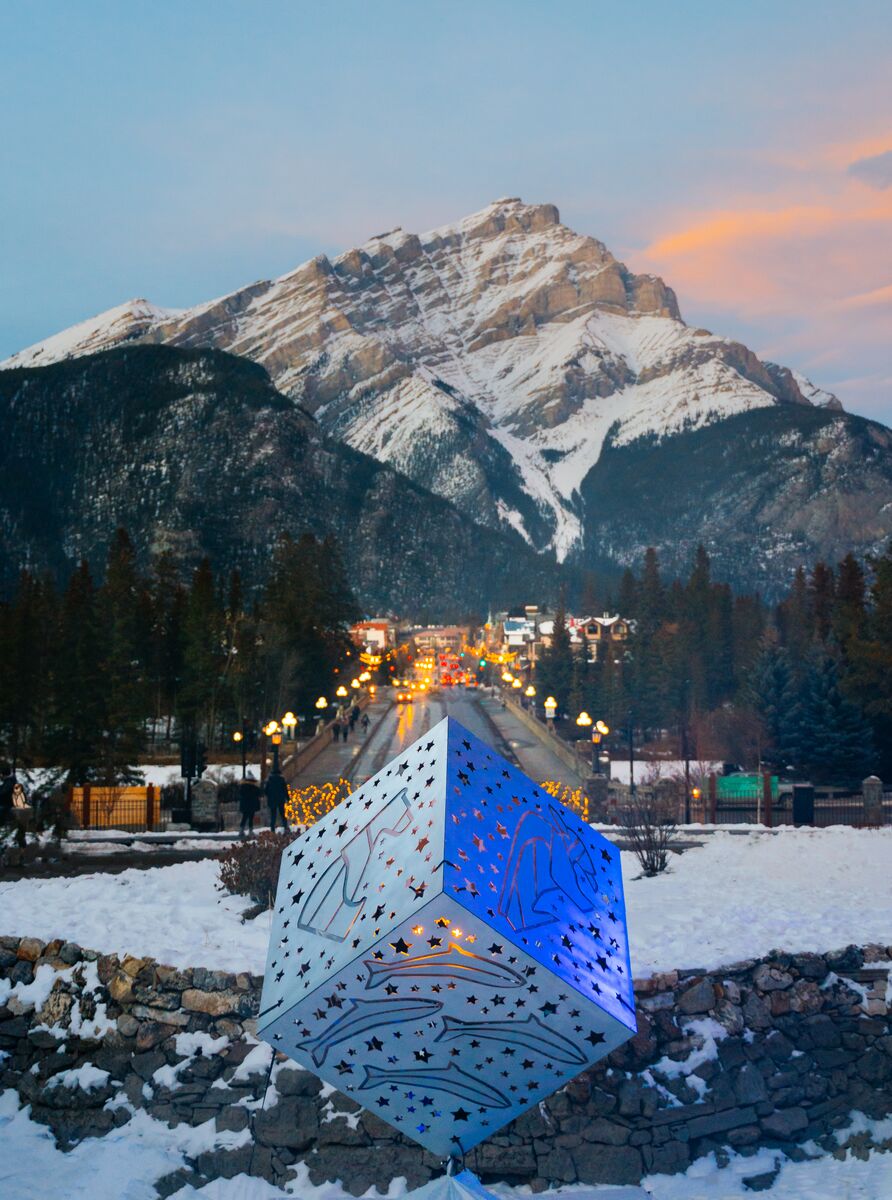 The cube for In Search of Christmas Spirit sits in the foreground with Banff Ave stretching out behind it towards Cascade Mountain in Banff National Park.